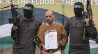 Israeli captive, Eli Sharabi, who has been held hostage by Hamas in Gaza since October 7, 2023, stands on a stage escorted by Hamas fighters before being handed over to the Red Cross.
