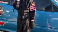 Girl in racing suit standing by blue car.
