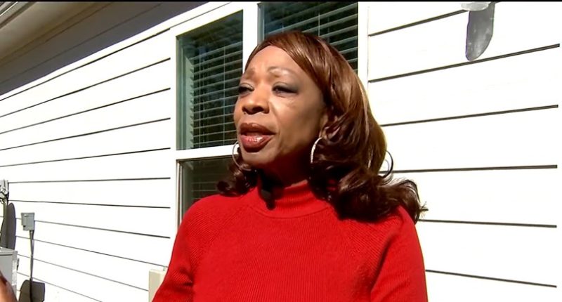 Woman in red sweater speaking outside a house.
