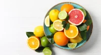 Different cut and whole citrus fruits on white wooden table, top view. Space for text