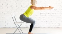 Yoga with a chair. Fit adult caucasian woman practice squat with props on a mat in loft white studio indoor, selective focus. Fitness, workout, trainer, sport, healthy lifestyle, concept.