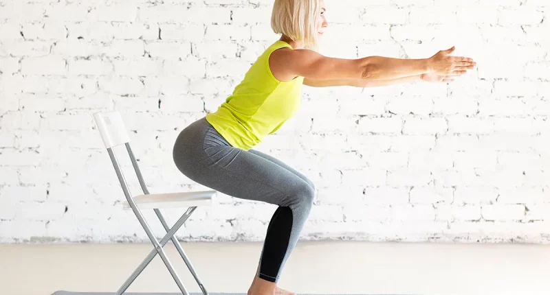 Yoga with a chair. Fit adult caucasian woman practice squat with props on a mat in loft white studio indoor, selective focus. Fitness, workout, trainer, sport, healthy lifestyle, concept.