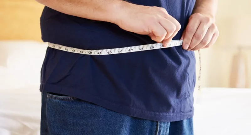 Close Up Of Overweight Man Measuring Waist