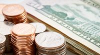 Stacks of pennies, nickels, and quarters with a stack of US dollar bills in the background.