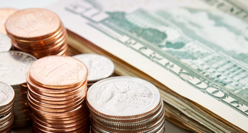 Stacks of pennies, nickels, and quarters with a stack of US dollar bills in the background.