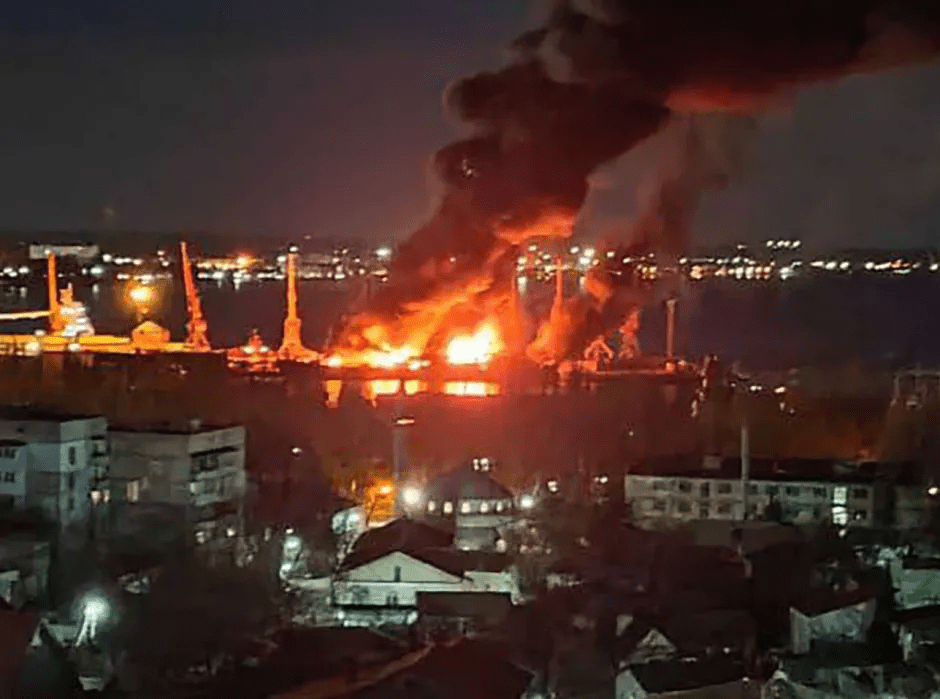 Large fire engulfing a structure near a body of water at night.