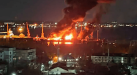 Large fire engulfing a structure near a body of water at night.