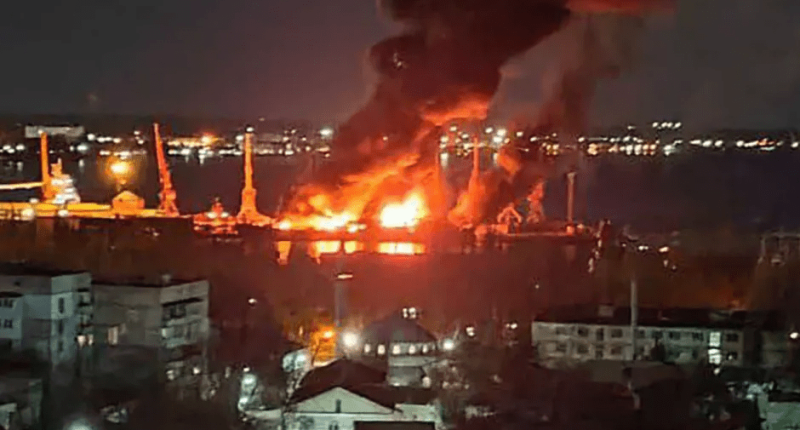 Large fire engulfing a structure near a body of water at night.