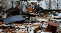 Debris from a tornado-damaged mobile home with a woman searching through it.