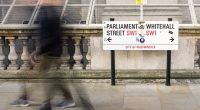 A blurred person walks past a street sign for Parliament Street and Whitehall in London.