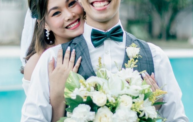 Newly married couple embracing, holding a bouquet.