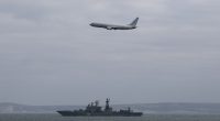 Airplane flying over a warship at sea.