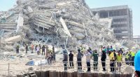 People stand near a collapsed building after an earthquake.