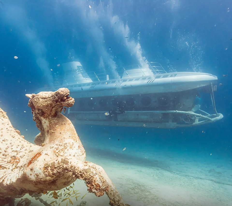 Underwater view of a submarine passing an ancient statue.