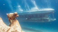 Underwater view of a submarine passing an ancient statue.