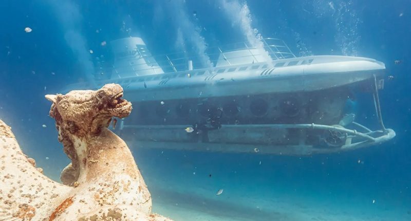 Underwater view of a submarine passing an ancient statue.