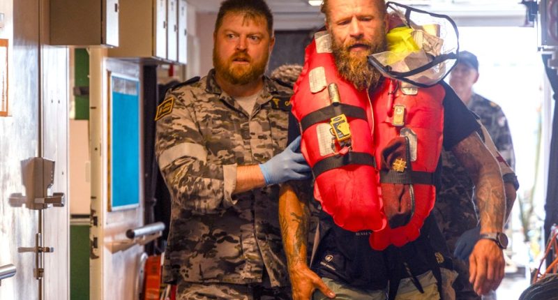 A navy medic assists a rescued long-distance rower aboard a ship.