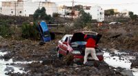A person inspects a damaged car after a flood.