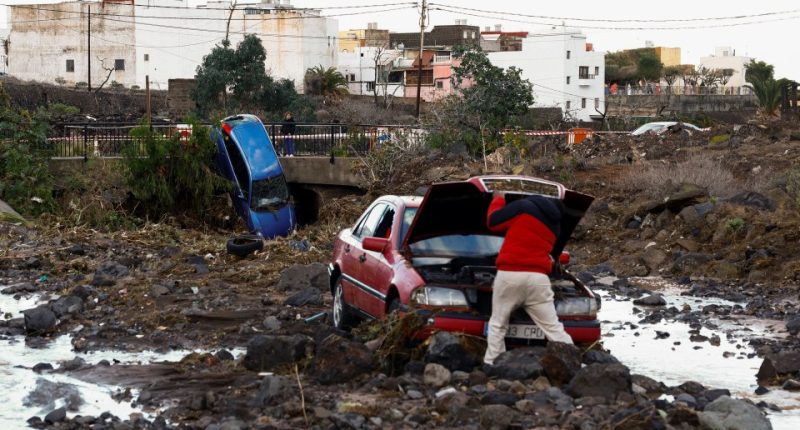 A person inspects a damaged car after a flood.