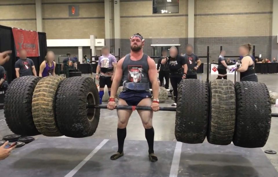 A strongman competitor lifting heavy tires during a competition.