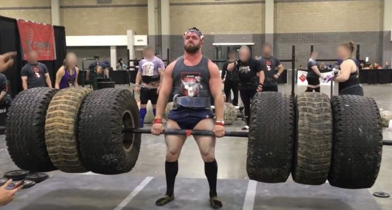 A strongman competitor lifting heavy tires during a competition.