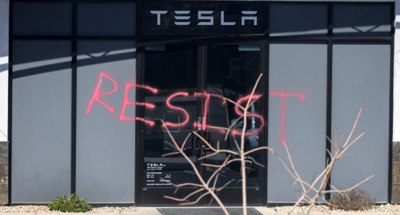 Graffiti reading "RESIST" on a Tesla Collision Center's glass doors.