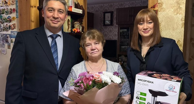 A woman receives a meat grinder and flowers from two people.