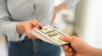 Close-up of a woman handing a stack of dollar bills to another person.