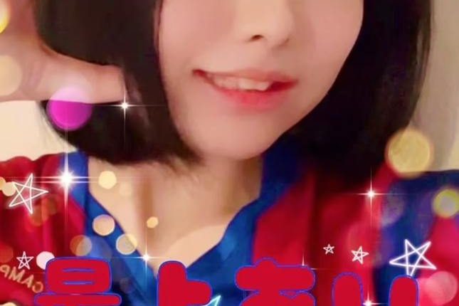 Screenshot of a woman in a red and blue jersey, making a heart shape with her hands.  Japanese text overlays the image.