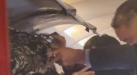 Passengers and crew dousing a burning bag in an airplane's overhead compartment.