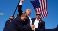 a man in a suit stands in front of an american flag