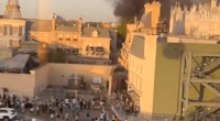 Smoke billowing over a park with people evacuating.