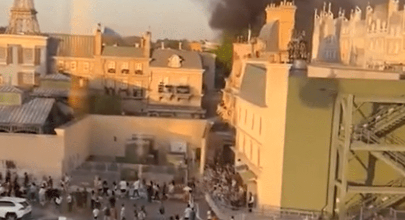 Smoke billowing over a park with people evacuating.