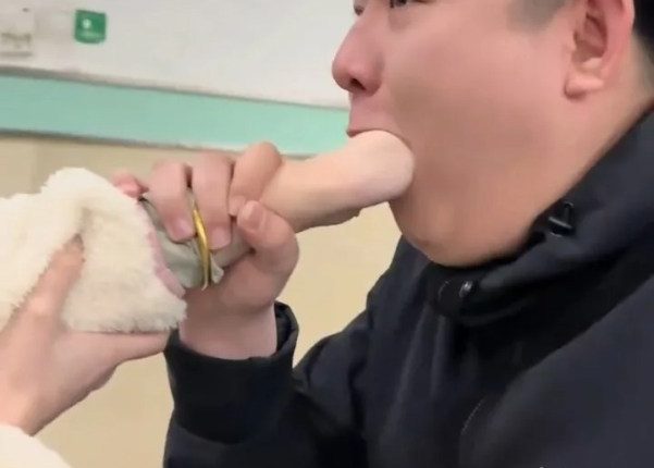 Video still of a woman's hand stuck in a man's mouth in a hospital waiting room.