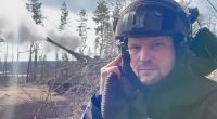 Screengrab of a man in a helmet near a firing AS90 gun.