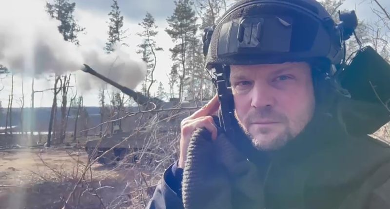 Screengrab of a man in a helmet near a firing AS90 gun.