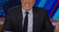 Jon Stewart on The Daily Show, holding a mug that says "World's Worst Dad."