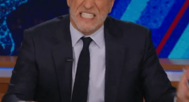Jon Stewart on The Daily Show, holding a mug that says "World's Worst Dad."