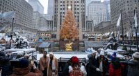 People taking photos of the Rockefeller Center Christmas tree in the snow.