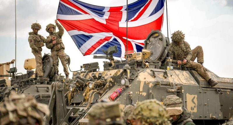 British soldiers on a military vehicle unfurl the Union Jack during a NATO exercise.