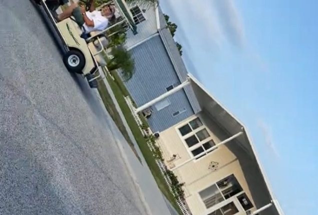 Man in golf cart on residential street.