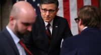 Man in suit and glasses speaking with colleagues before a congressional address.