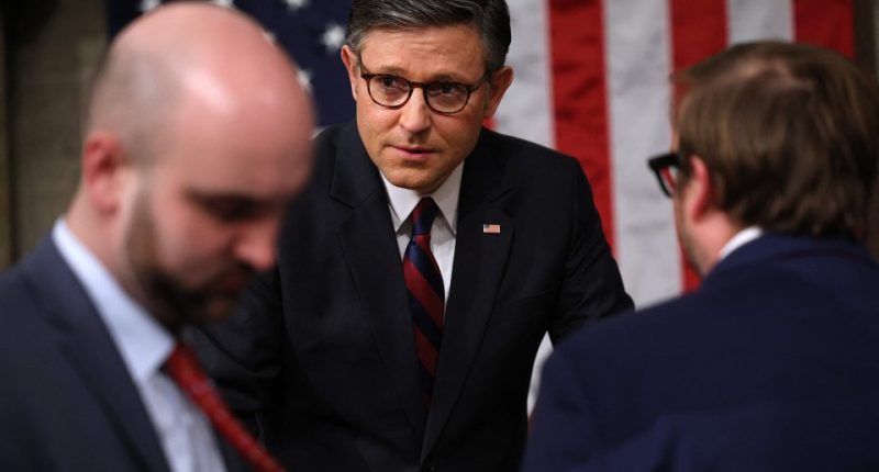 Man in suit and glasses speaking with colleagues before a congressional address.