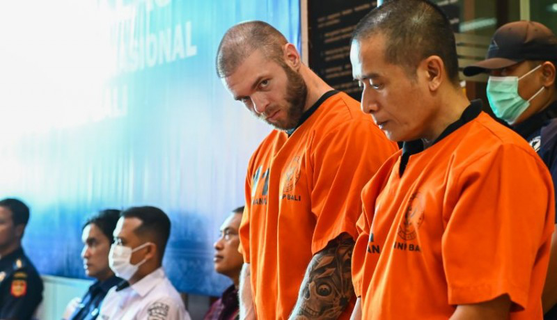 A British man in an orange prison jumpsuit stands with Indonesian police officers.