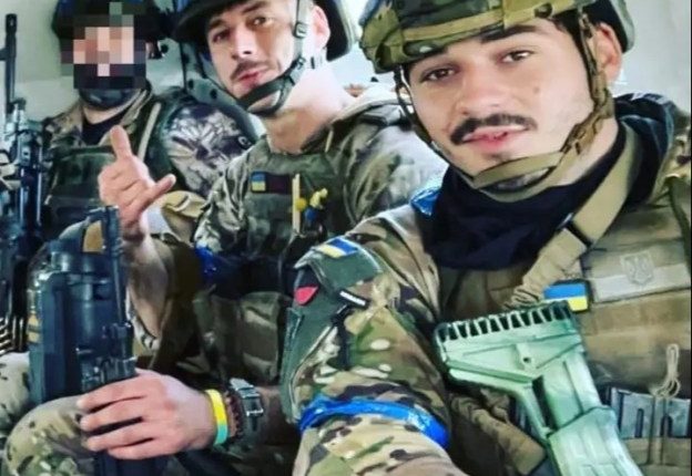 Three Ukrainian soldiers in camouflage uniforms and helmets inside a military vehicle.