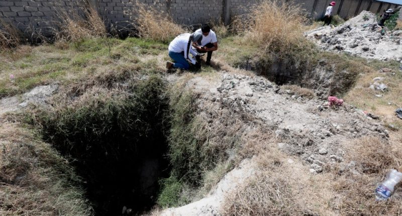 Two people examining a pit at a crime scene.
