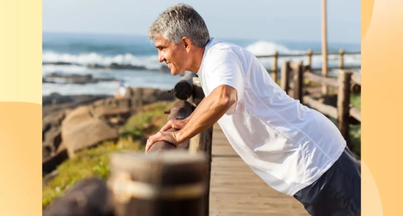 fit senior man doing incline pushups on a beach walk railing