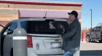 A man placing a note on the back of a car at a gas station.