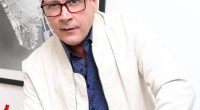 Portrait of a man wearing glasses and a light beige jacket.