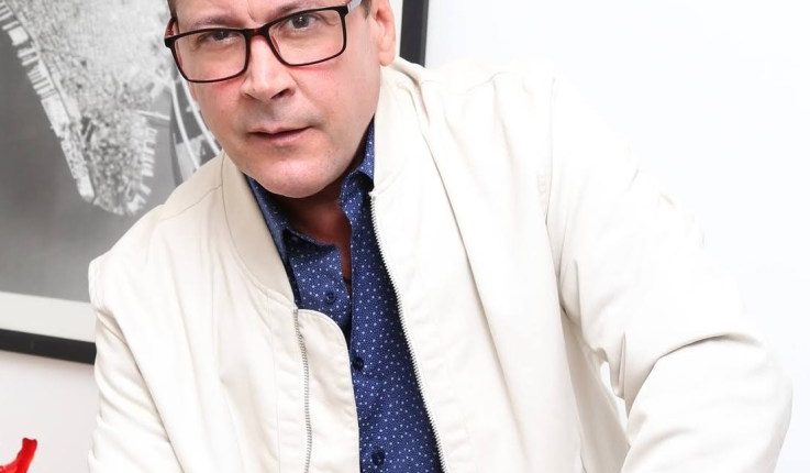 Portrait of a man wearing glasses and a light beige jacket.